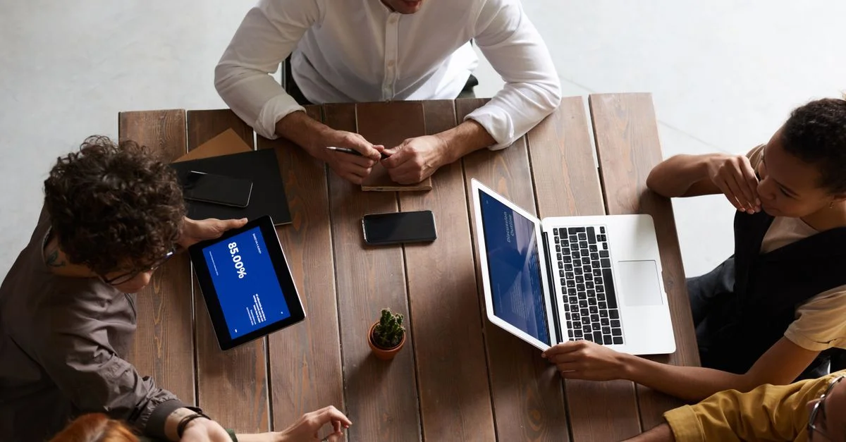 Vue de dessus d'une équipe diversifiée collaborant avec des ordinateurs portables et des tablettes dans un espace de travail moderne.