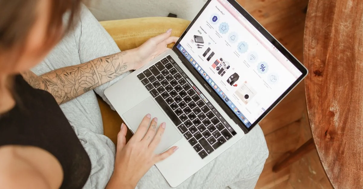Femme tatouée consultant un site de shopping en ligne sur un ordinateur portable à l'intérieur